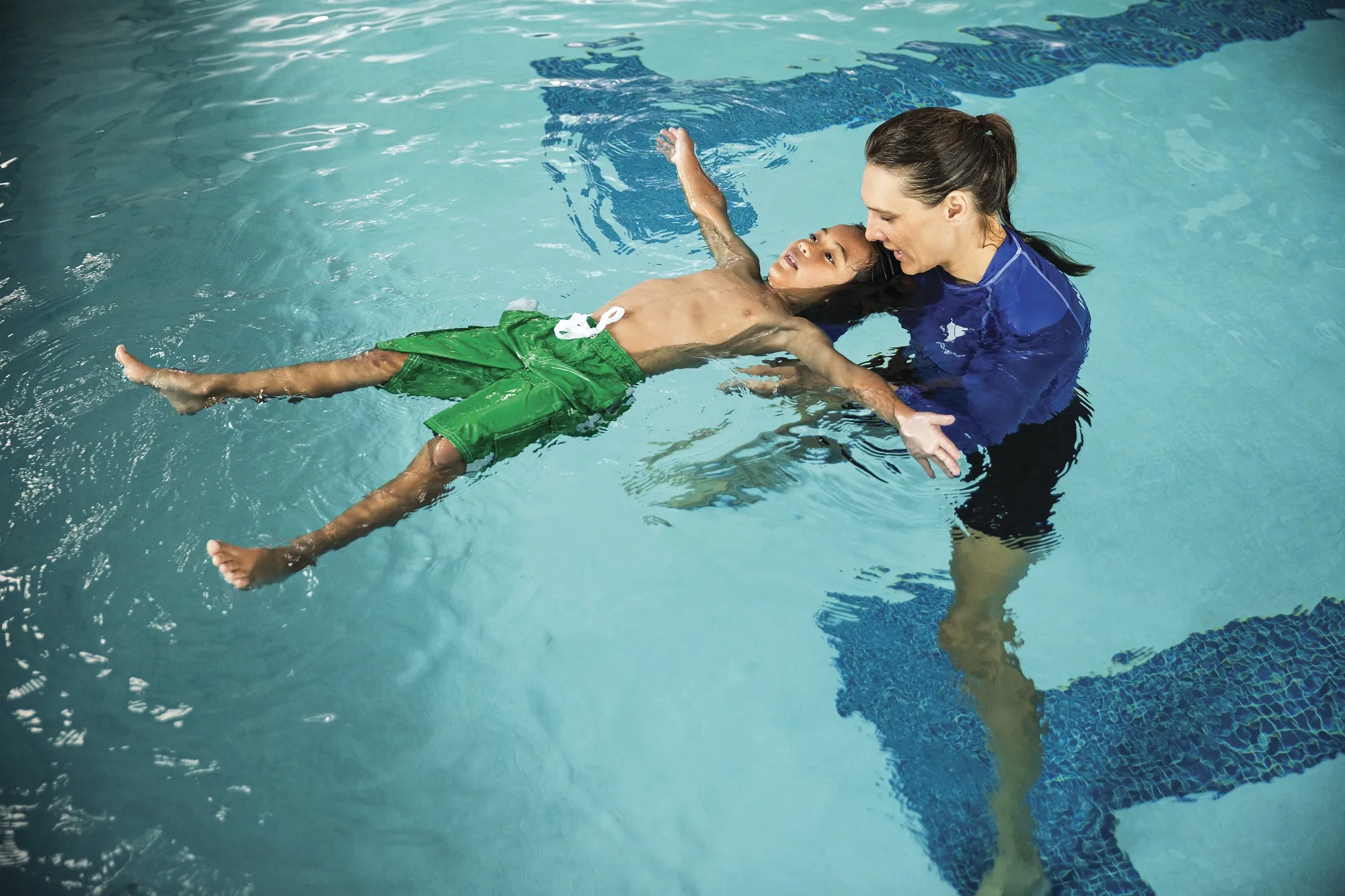 Swim instructor teaching a kid to float on his back.